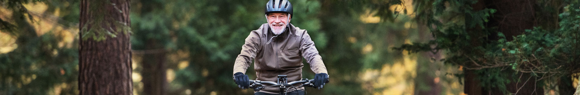 A senior man biking on a forested path in the fall