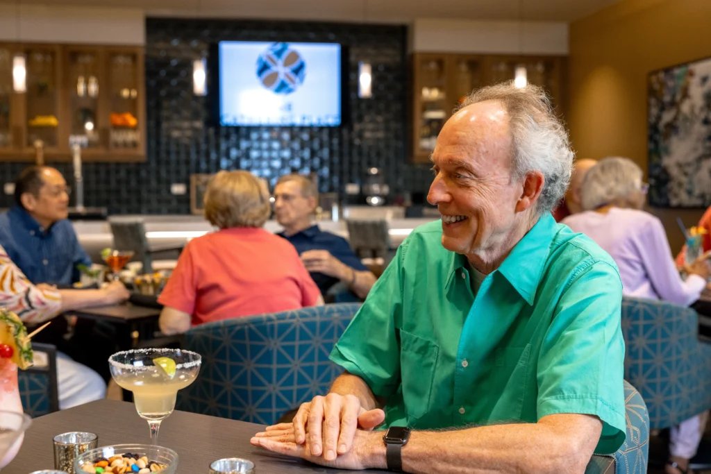 senior man sitting at table with other seniors in the background at Monarch Landing lounge
