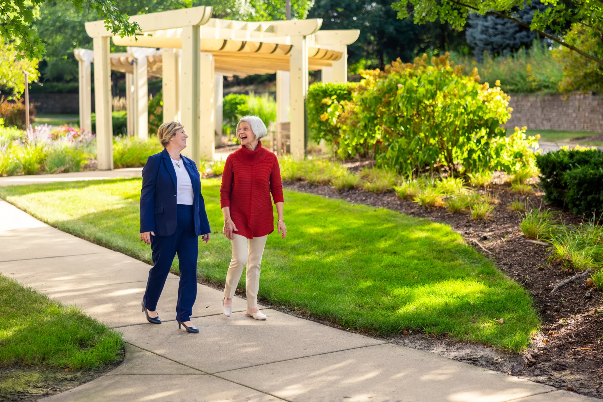 Two senior women walking on a sidewalk and talking about the benefits of a life plan community in Naperville, Illinois at Monarch Landing.